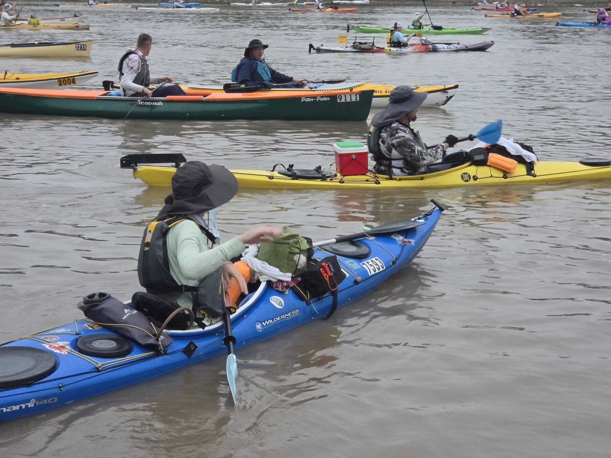 Loretta Harris, foreground, paddles her blue kayak among competitors during the 2026 MR340 as Jason Richardson follows in his yellow kayak.